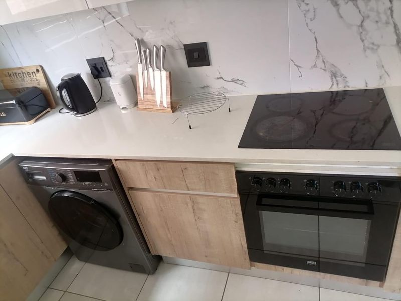 Modern kitchen featuring marble-look splashback, quartz countertops, built-in oven with electric hob, and integrated under-counter laundry space.