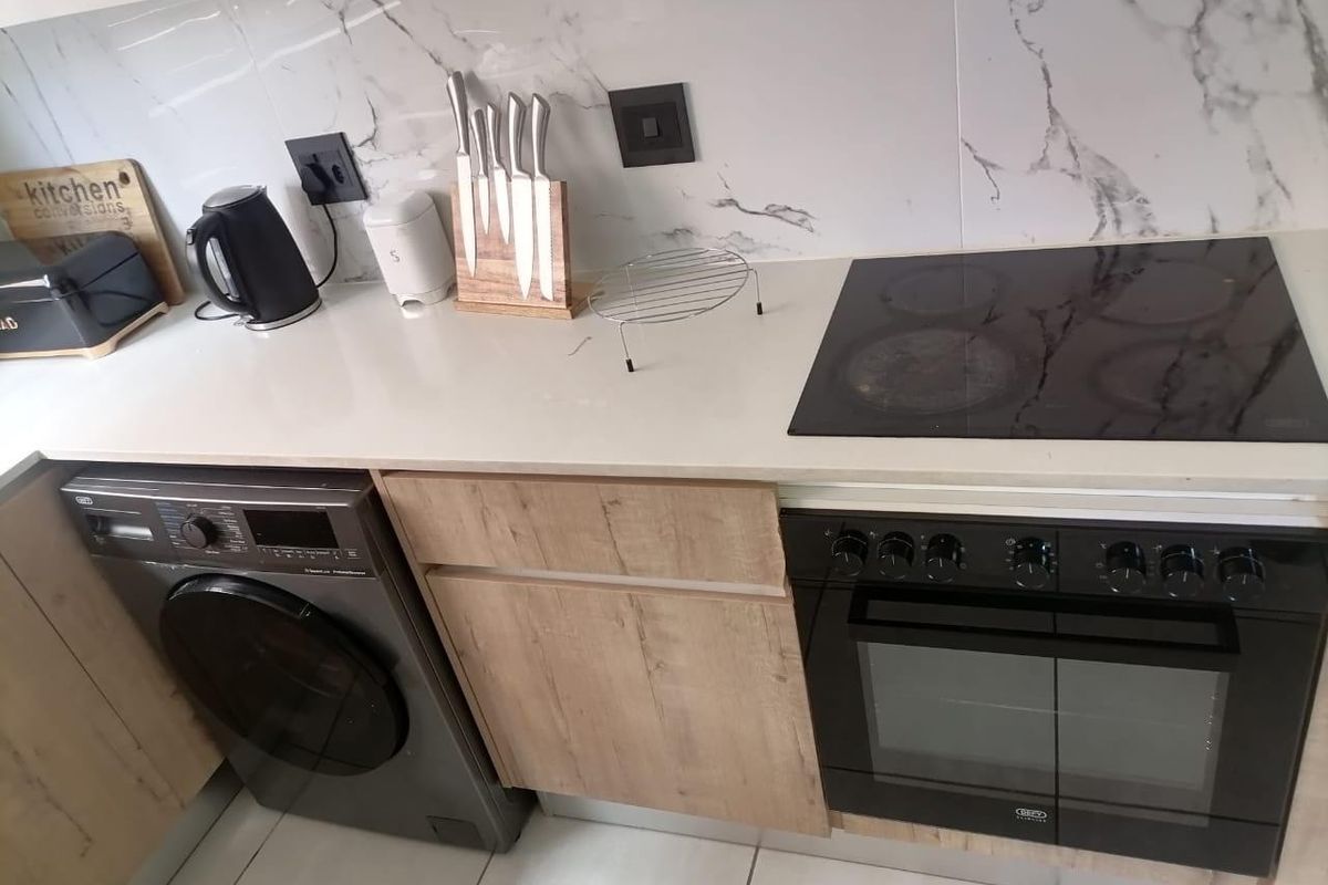 Modern kitchen featuring marble-look splashback, quartz countertops, built-in oven with electric hob, and integrated under-counter laundry space.