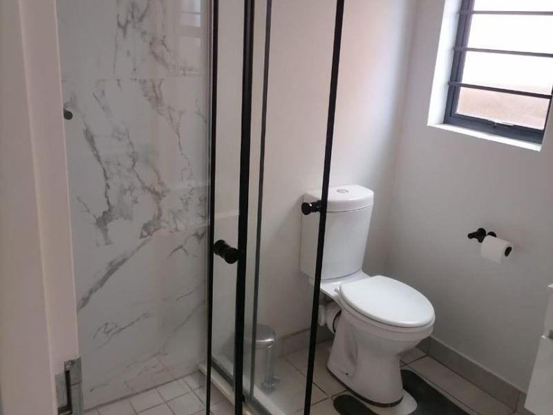 A modern bathroom featuring a walk-in shower with black-framed glass enclosure, marble-look wall tiling, and a standard toilet.
