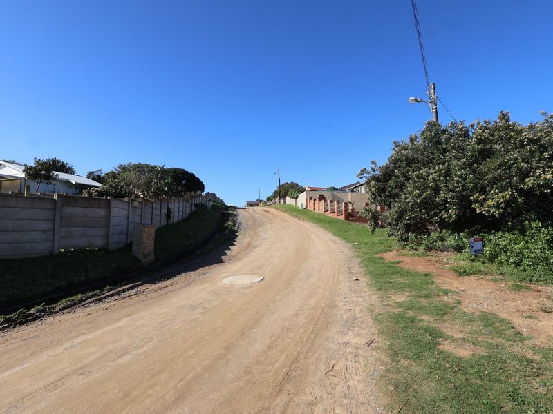 A view of the unpaved street access leading to the residential vacant land, featuring established boundary walls and utility infrastructure.