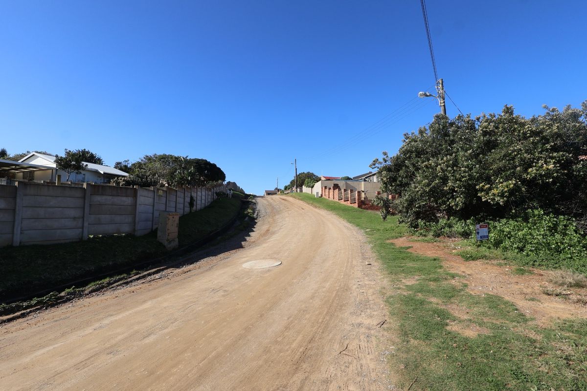 A view of the unpaved street access leading to the residential vacant land, featuring established boundary walls and utility infrastructure.