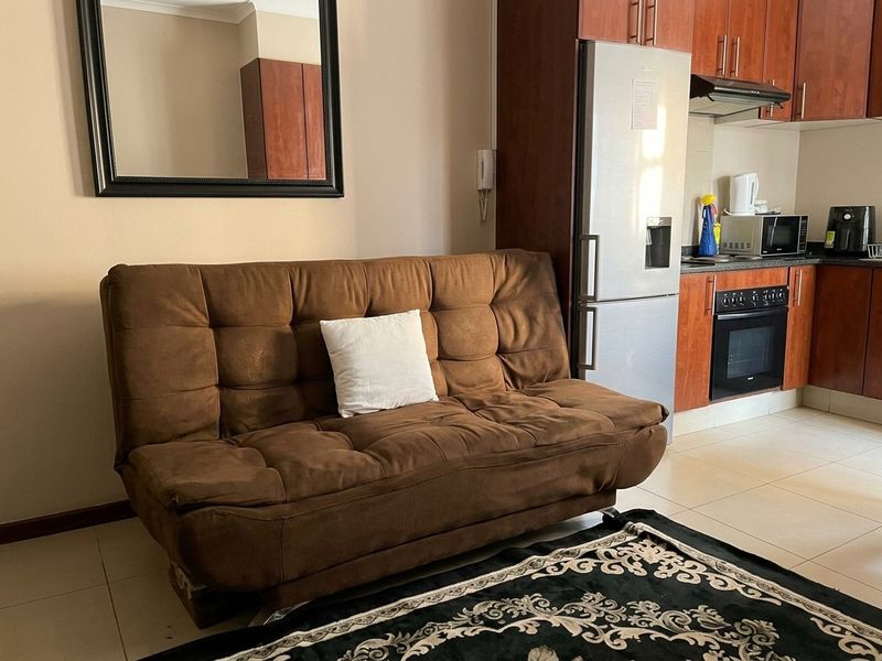 Open plan living area featuring a compact kitchen with built-in cabinetry, oven, and hob, finished with neutral tiled flooring.