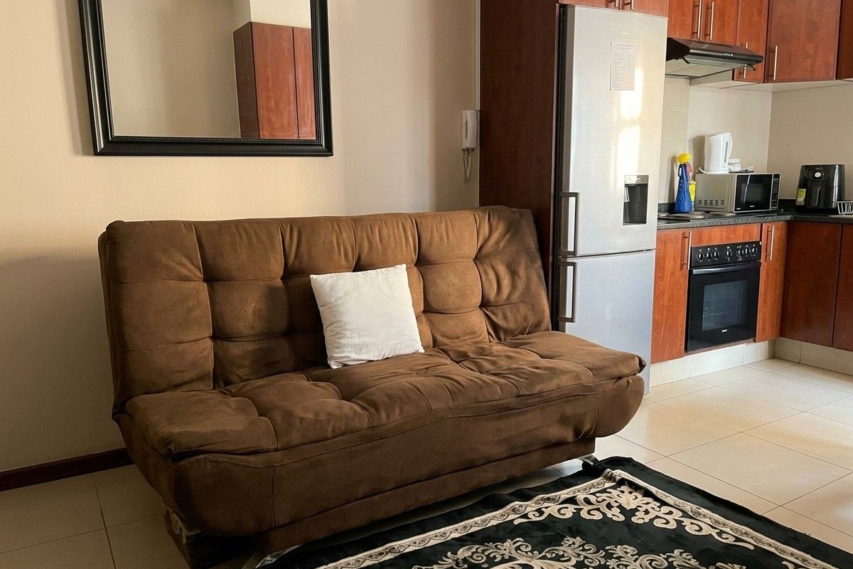 Open plan living area featuring a compact kitchen with built-in cabinetry, oven, and hob, finished with neutral tiled flooring.