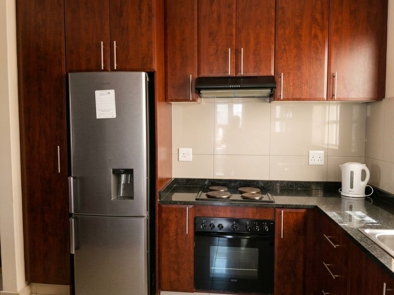 A functional kitchen featuring dark wood cabinetry, granite countertops, a built-in oven, electric hob, and a tiled splashback.