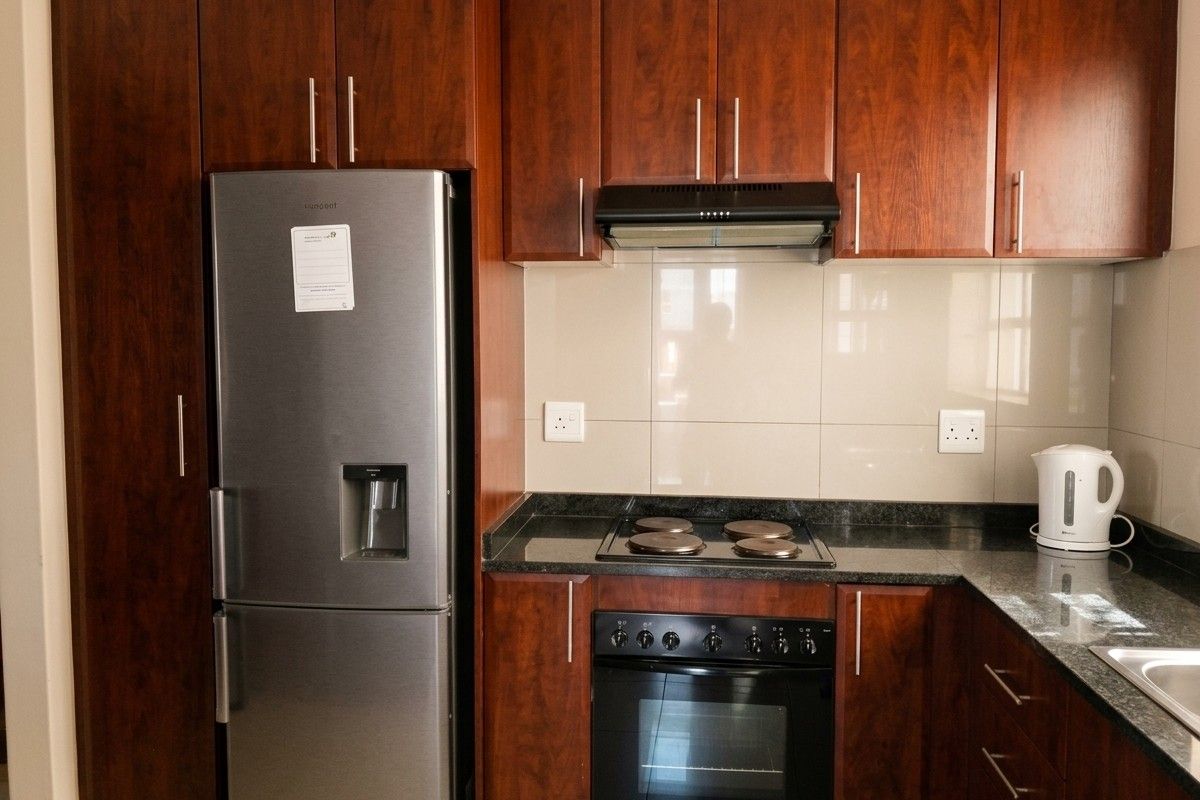 A functional kitchen featuring dark wood cabinetry, granite countertops, a built-in oven, electric hob, and a tiled splashback.
