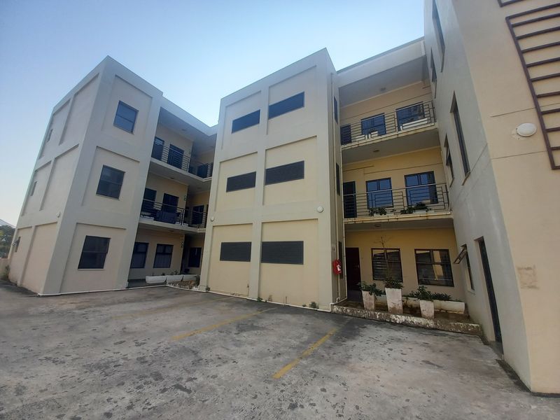 Exterior view of a multi-story apartment complex featuring concrete parking area, balconies with metal railings, and functional exterior building finishes.