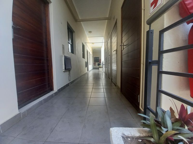 A clean, tiled apartment hallway featuring multiple wooden doors and a metal safety balustrade.