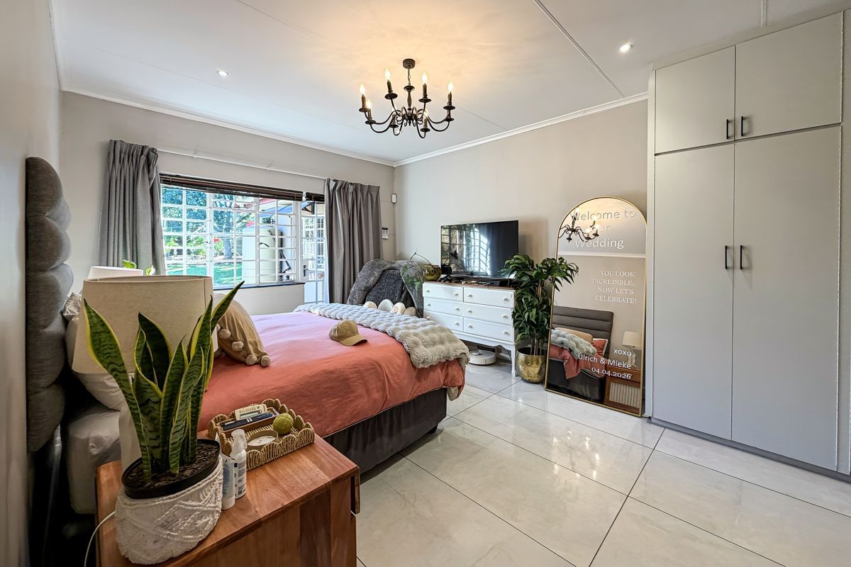 A well-maintained bedroom featuring tiled flooring, built-in cupboards, and a decorative chandelier, with direct access to the garden through a security gate.