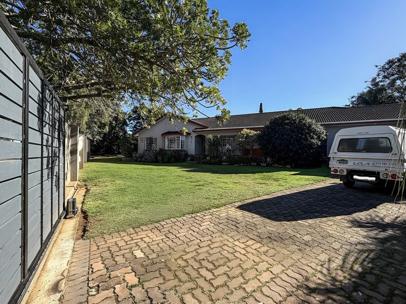 Front view of the property featuring a paved driveway, well-maintained lawn, and a single-story house with a tiled roof.