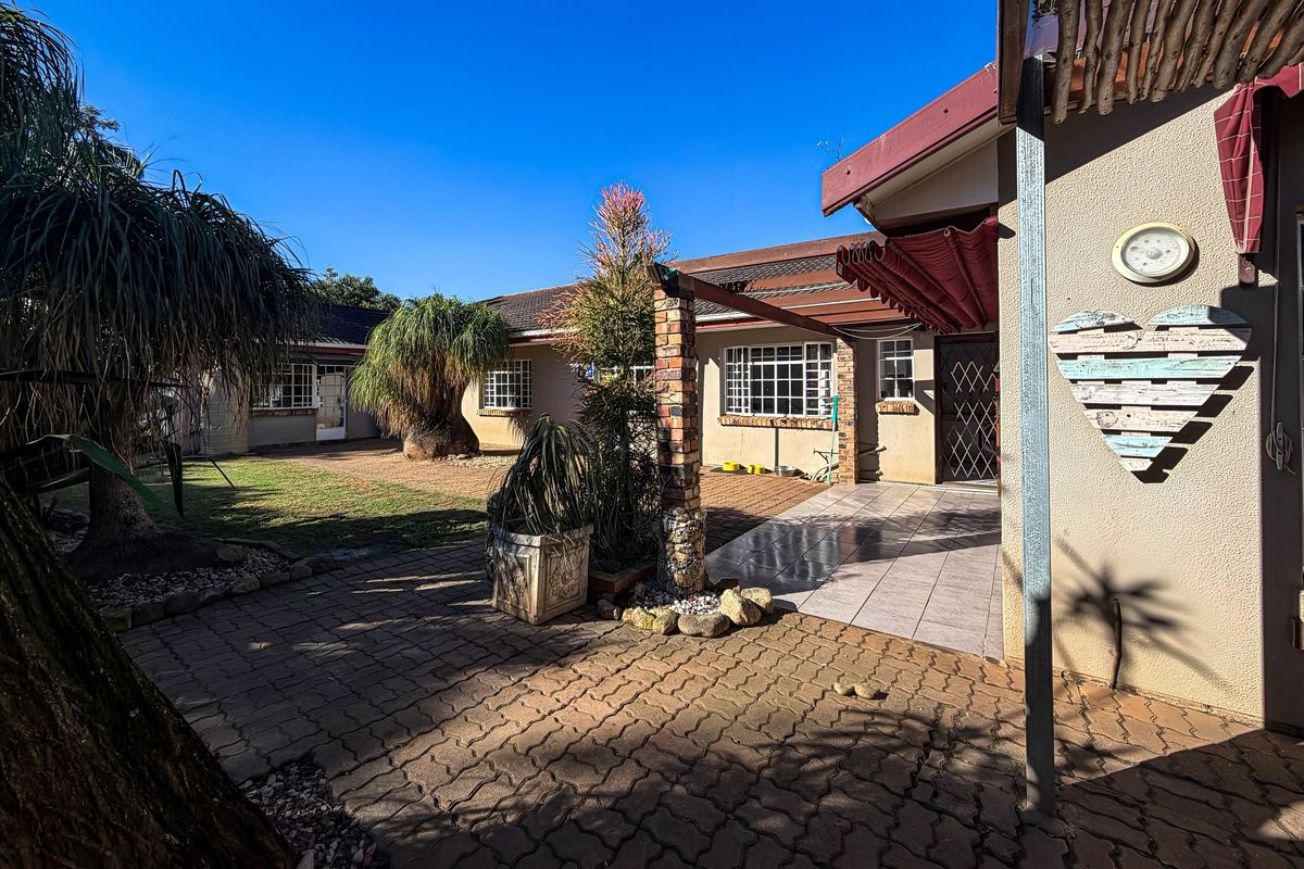A rear exterior view featuring a paved courtyard, tiled patio area, and established garden space with brick structural elements.