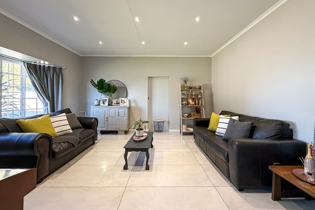 A well-maintained living room featuring large format porcelain floor tiles, recessed downlighting, and neutral wall finishes.