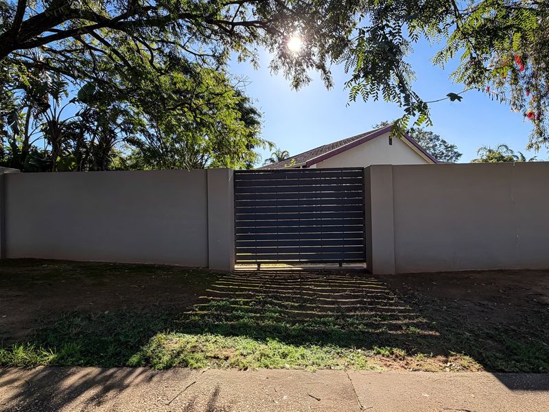 Front view of the property featuring a solid perimeter wall and a modern horizontal slat sliding gate, with a tiled roof visible in the background.
