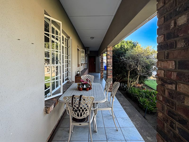 A covered outdoor patio area featuring tiled flooring and exposed brick pillars, providing a functional space for outdoor relaxation and garden views.