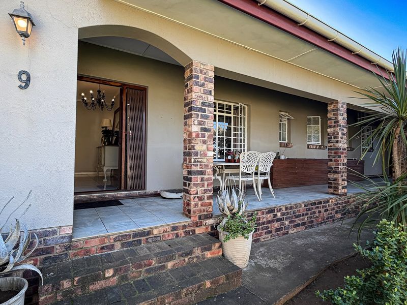 A covered front patio featuring brick pillars, tiled flooring, and a secure entrance, providing a welcoming outdoor space for the home.