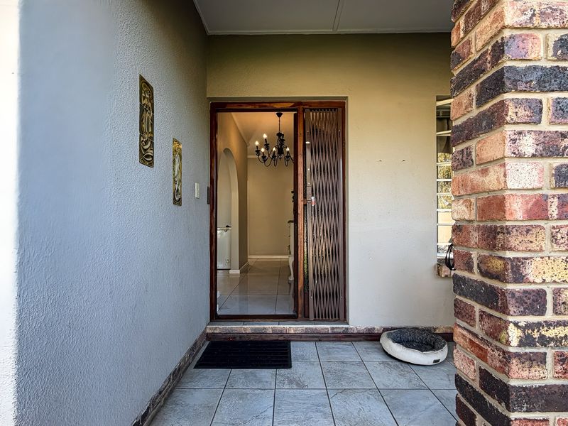 Covered entrance porch featuring a brick pillar, tiled flooring, and a security gate leading into the home.