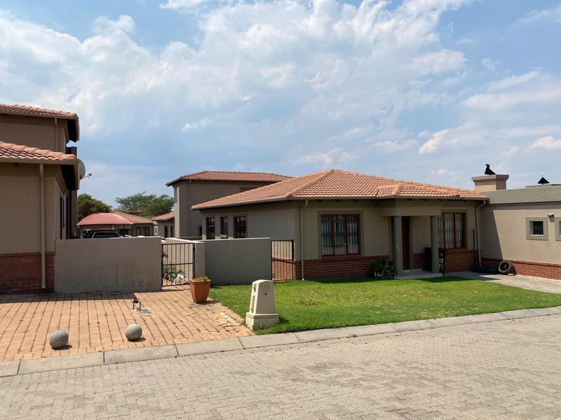 Front view of a single-story residential house featuring a tiled roof, brick accents, paved driveway, and a small front lawn.