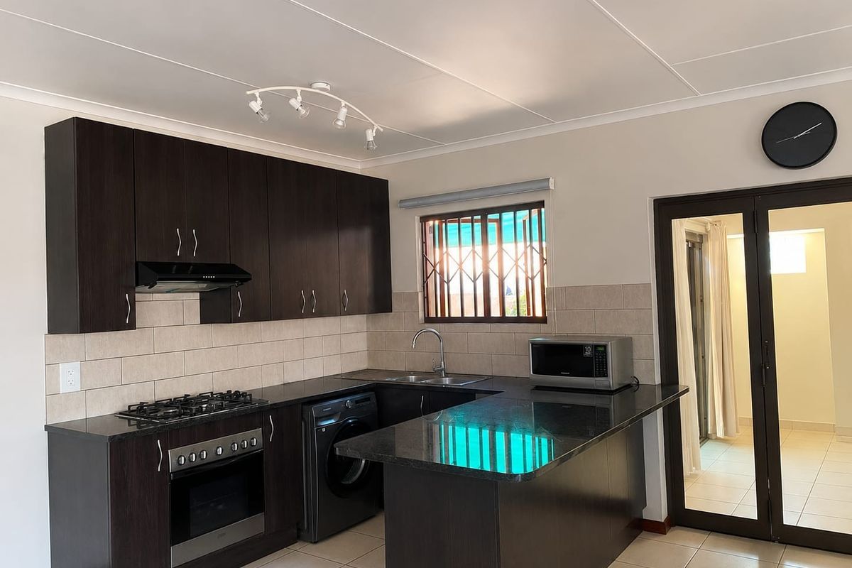 Modern kitchen featuring dark wood cabinetry, granite countertops, built-in oven, gas hob, and tiled flooring with a functional layout.