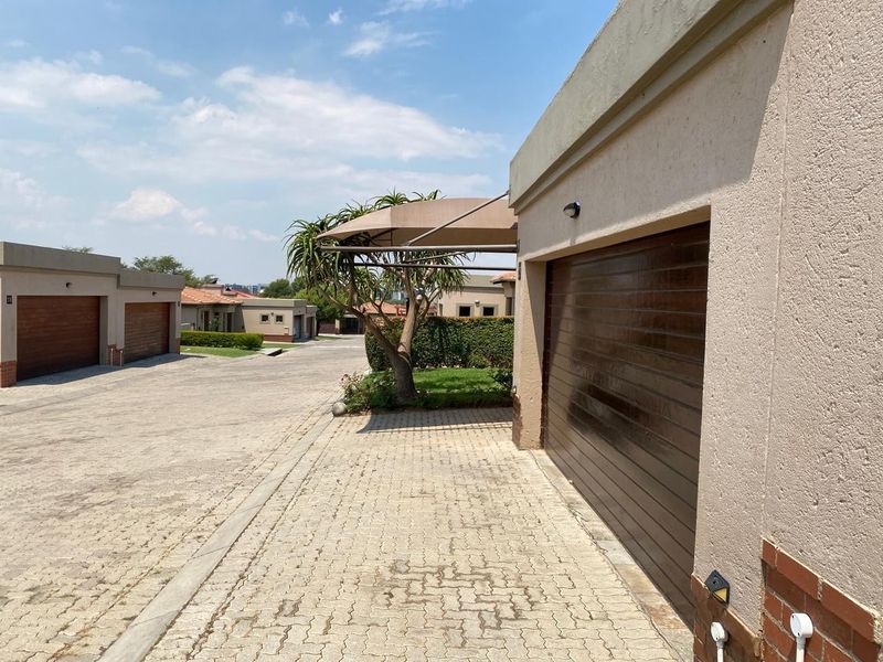 A view of the paved driveway and garage entrance in a residential estate, featuring well-maintained exterior finishes and a shade structure.