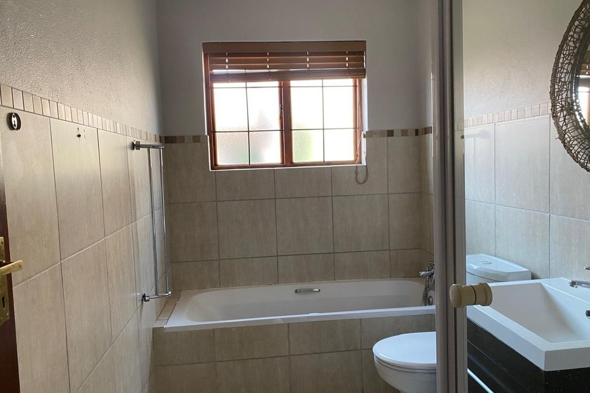 A functional bathroom featuring a built-in bathtub, toilet, and vanity basin with neutral wall tiling and natural light from a window.