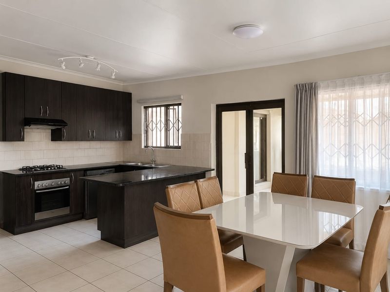 Open-plan kitchen and dining area featuring dark wood cabinetry, granite countertops, built-in appliances, and tiled flooring with direct access to the patio.