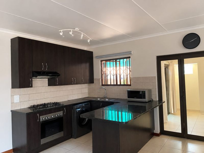 Modern kitchen featuring dark wood cabinetry, granite countertops, built-in oven, gas hob, and tiled flooring with a functional layout.