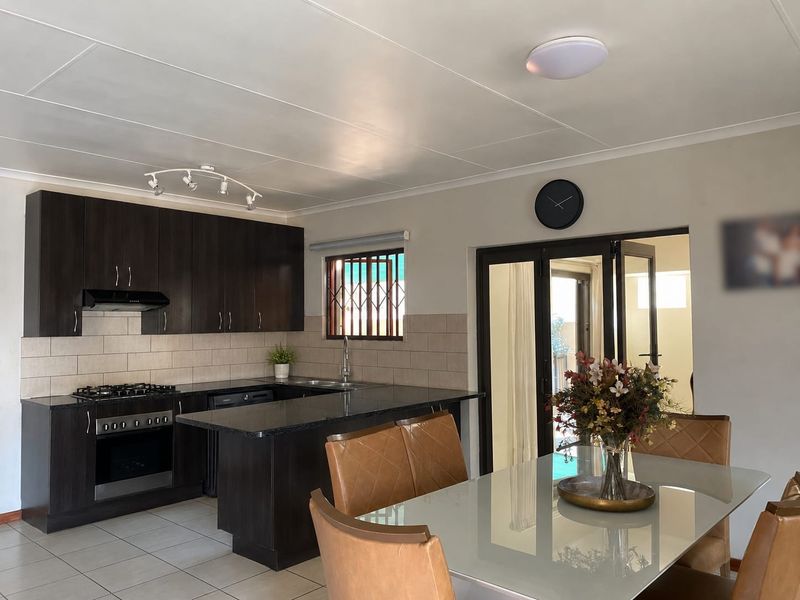 Open-plan kitchen and dining area featuring dark wood cabinetry, granite countertops, gas hob, and bi-fold doors leading to an outdoor space.