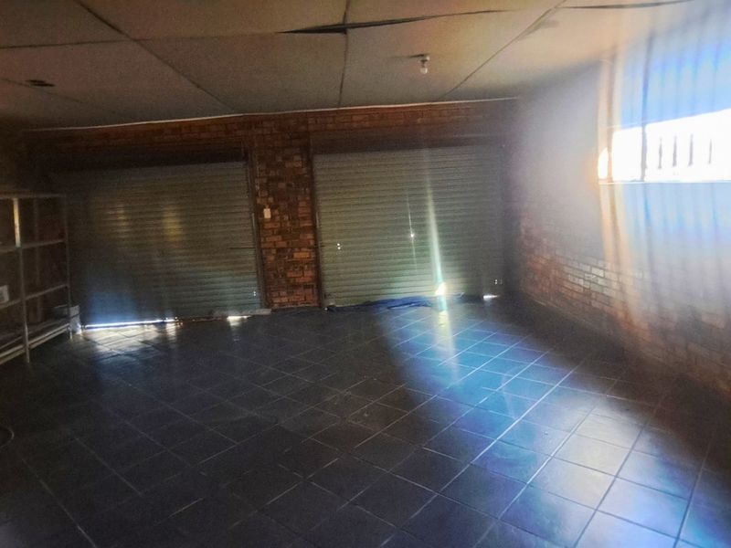 Spacious double garage featuring exposed brick walls, tiled flooring, and a drop ceiling, offering ample storage or vehicle parking space.
