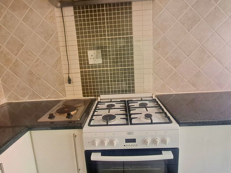 Kitchen area featuring a combination gas stove and electric hob, dark laminate countertops, and a decorative tiled backsplash.