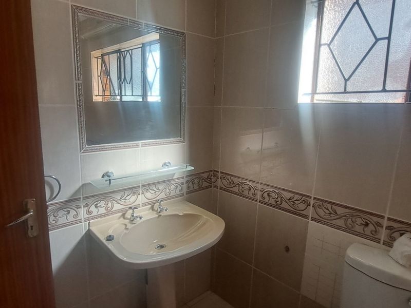 A dated bathroom featuring a pedestal basin, toilet, and ceramic wall tiles with a decorative border, requiring minor maintenance and cosmetic updates.