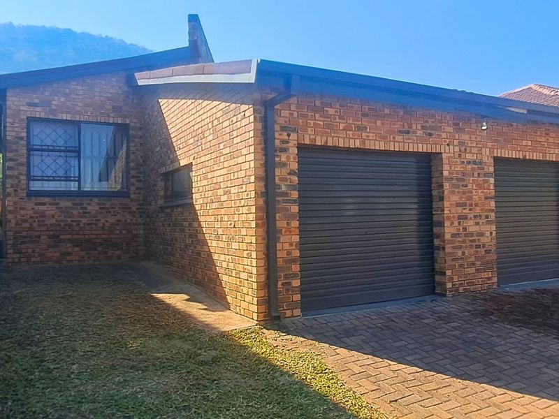 Front view of a face brick house featuring a double garage with roller shutter doors and a paved driveway.