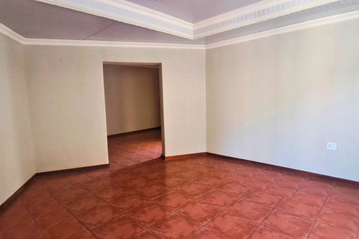 A spacious, empty living area featuring terracotta-style floor tiles, a tray ceiling with crown molding, and neutral wall finishes.