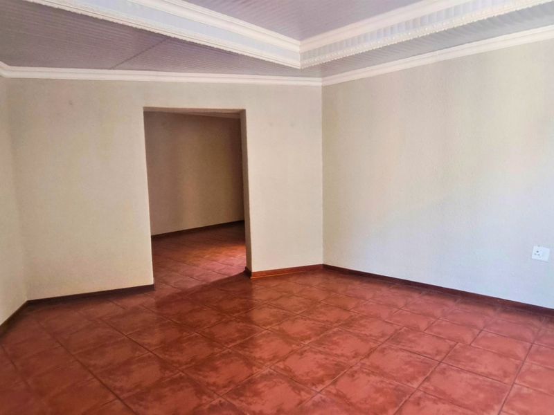 A spacious, empty living area featuring terracotta-style floor tiles, a tray ceiling with crown molding, and neutral wall finishes.