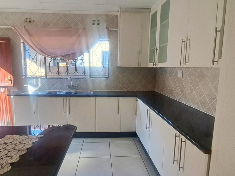 A functional kitchen featuring white cabinetry, dark countertops, tiled backsplash, and direct access to the exterior.