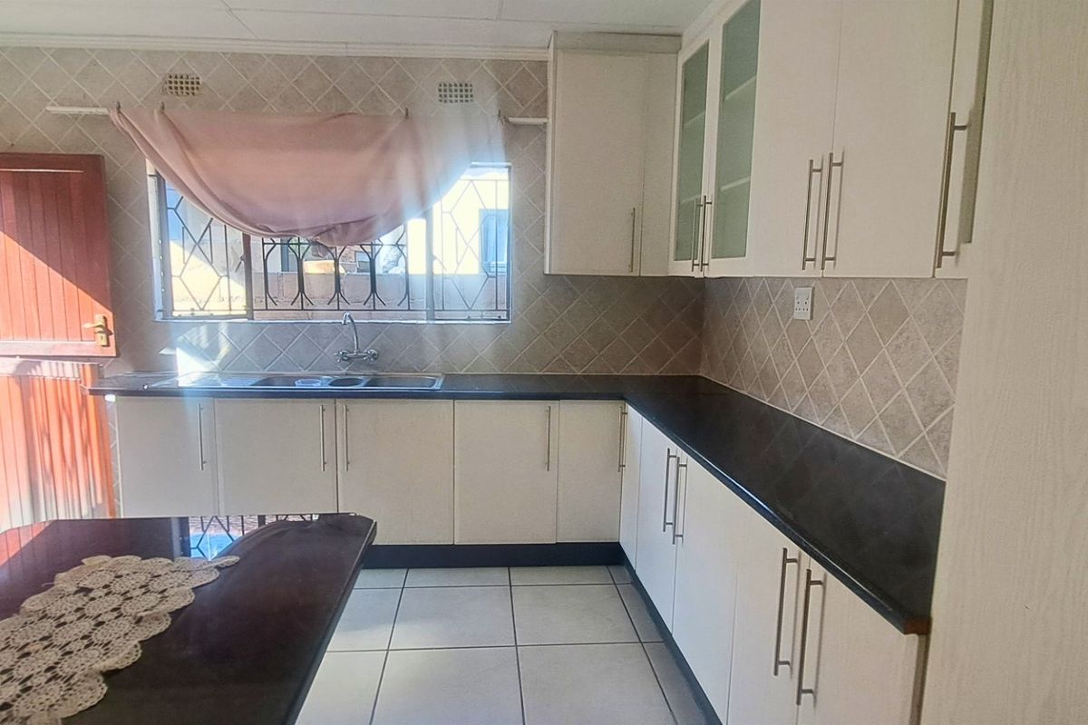 A functional kitchen featuring white cabinetry, dark countertops, tiled backsplash, and direct access to the exterior.