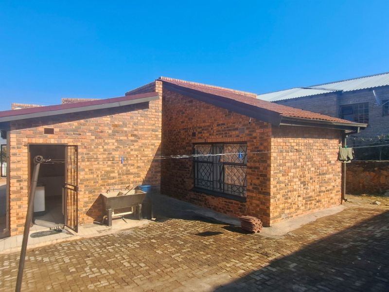 Rear view of a face brick house featuring a paved courtyard, security gate, and external wash trough area.