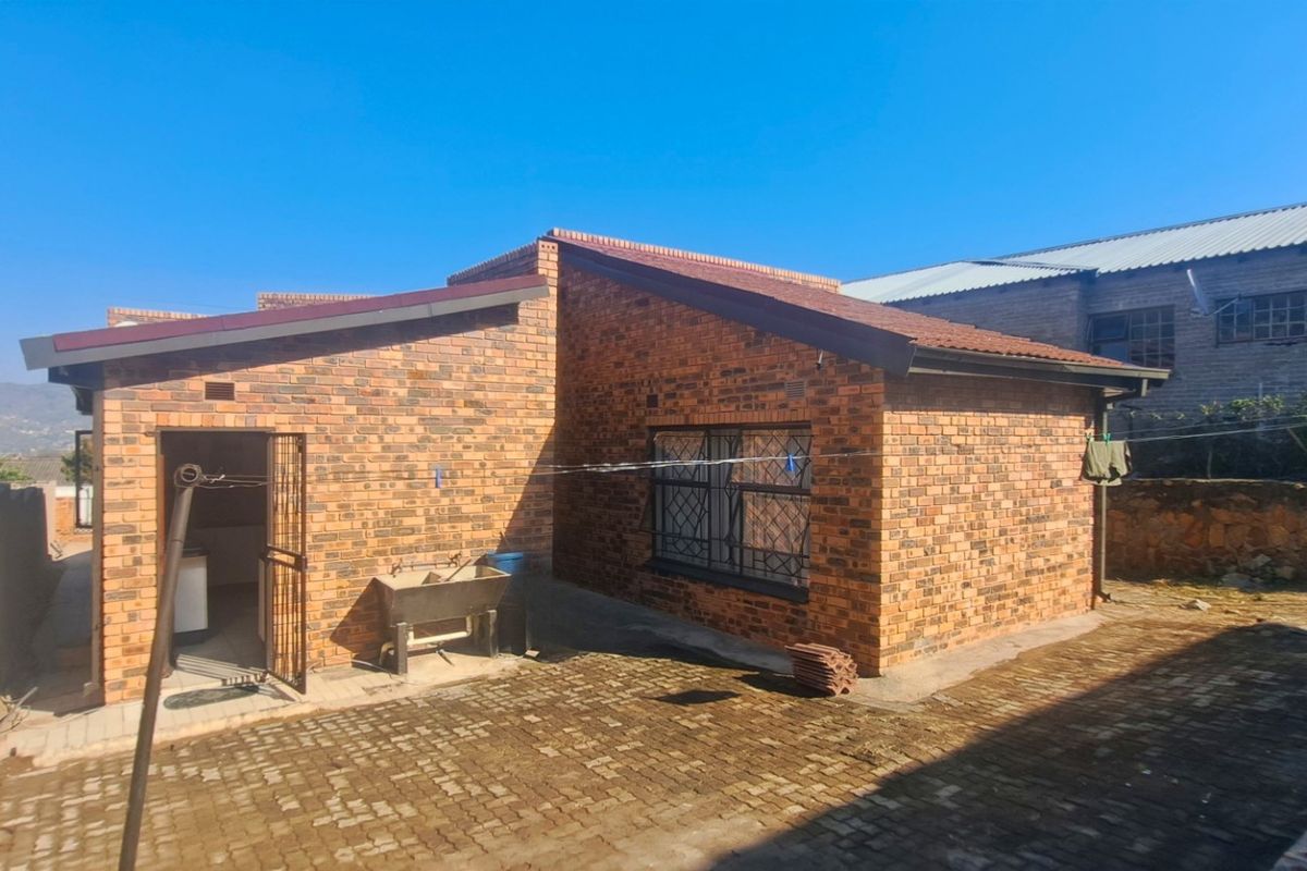 Rear view of a face brick house featuring a paved courtyard, security gate, and external wash trough area.
