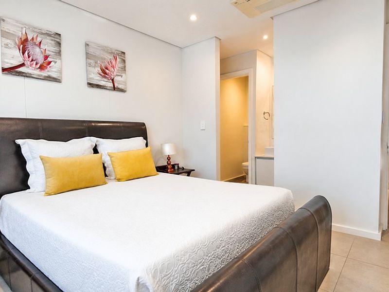 A well-maintained bedroom featuring neutral tiled flooring, recessed lighting, and direct access to an en-suite bathroom.