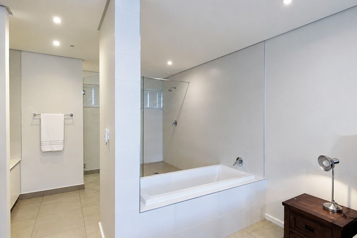 Modern open-plan bathroom featuring a built-in bathtub, glass-enclosed shower, and neutral tiled finishes, seamlessly integrated with the adjacent bedroom space.