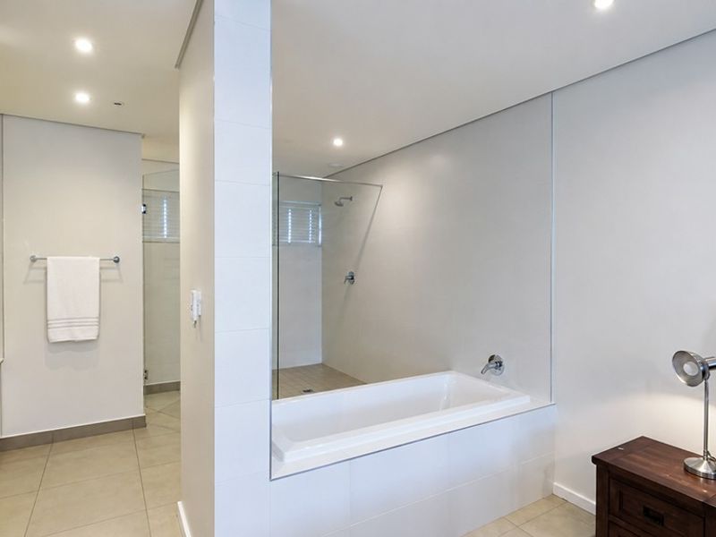 Modern open-plan bathroom featuring a built-in bathtub, glass-enclosed shower, and neutral tiled finishes, seamlessly integrated with the adjacent bedroom space.
