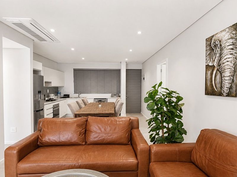 Modern open-plan living and kitchen area featuring sleek cabinetry, integrated appliances, recessed lighting, and ducted air conditioning in a well-maintained apartment setting.