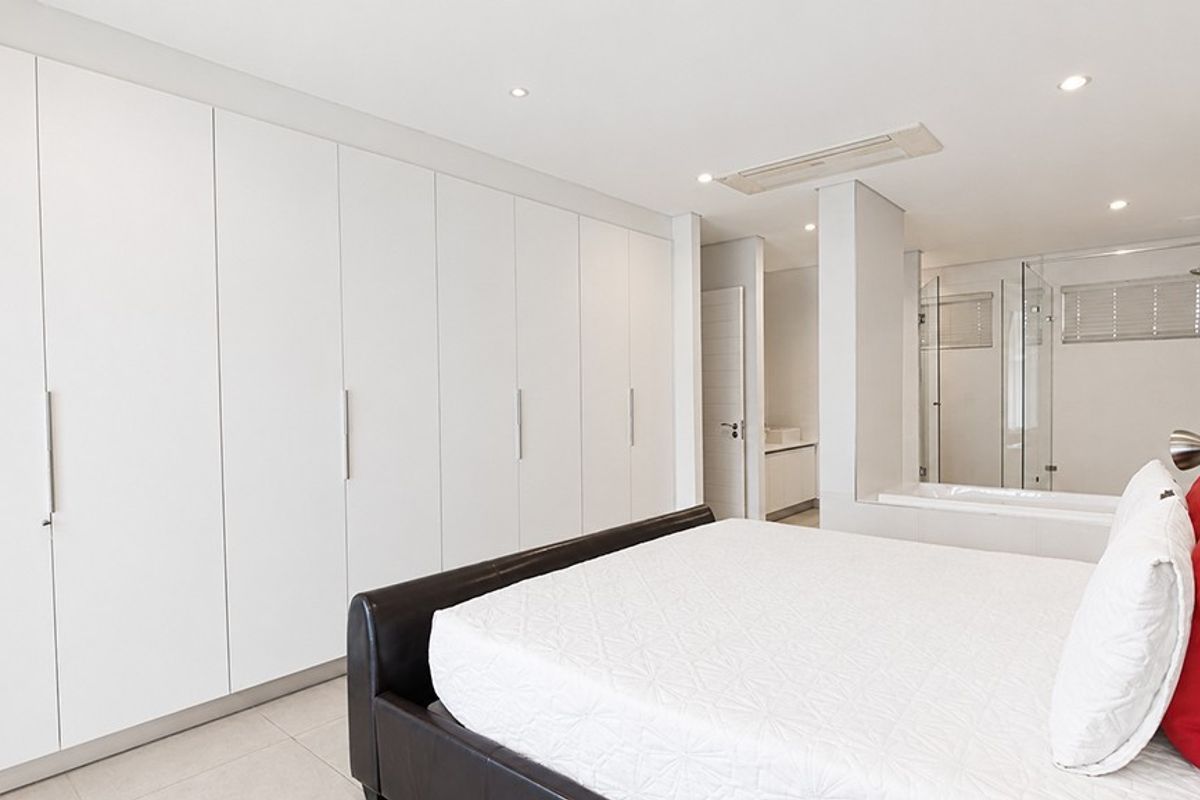 Spacious bedroom featuring extensive built-in cupboards, recessed lighting, ducted air conditioning, and an open-plan en-suite bathroom with a glass shower enclosure.