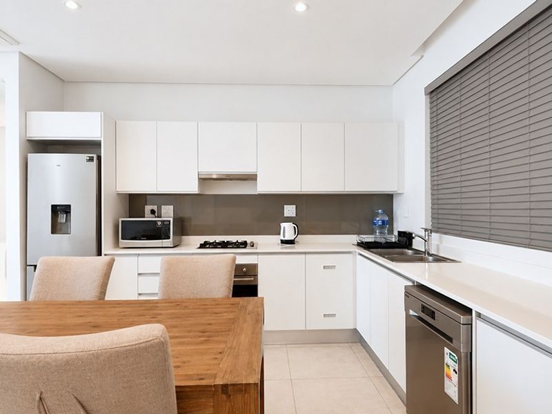Modern open-plan kitchen featuring sleek white cabinetry, integrated appliances, gas hob, and tiled flooring, seamlessly flowing into the dining area.