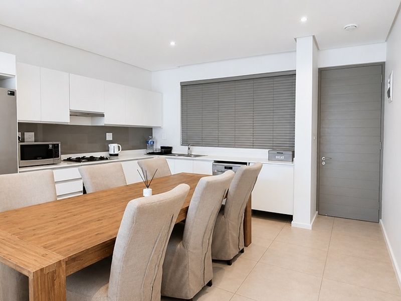 Modern open-plan kitchen and dining area featuring sleek white cabinetry, gas hob, integrated appliances, and neutral tiled flooring.