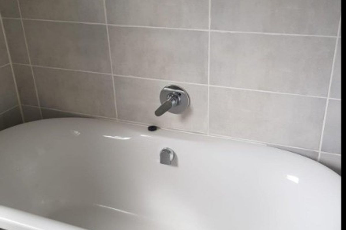 A clean, modern bathroom featuring a white freestanding bathtub with a wall-mounted chrome faucet and neutral ceramic wall tiling.