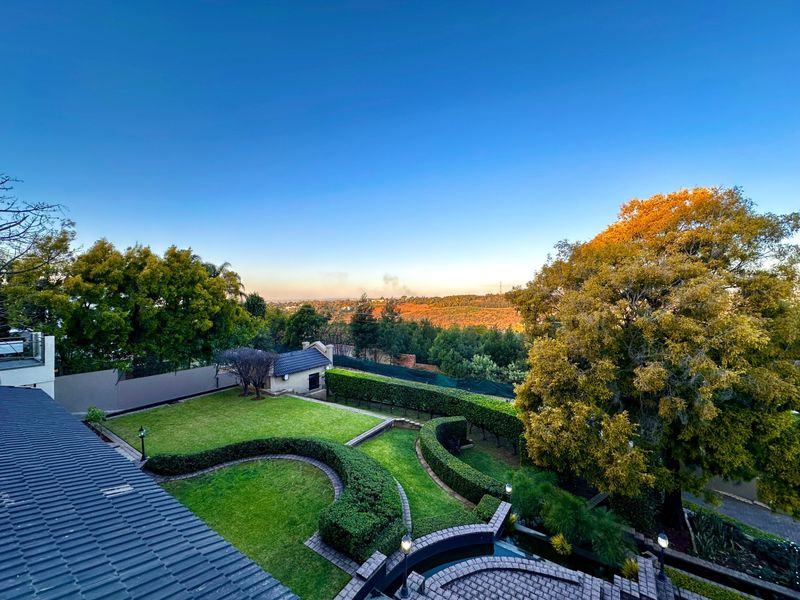 Elevated view overlooking a well-manicured garden with structured hedging, mature trees, and a scenic landscape backdrop.