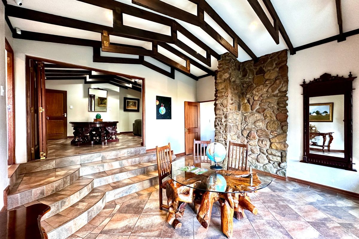 Spacious living area featuring a striking stone fireplace, exposed timber ceiling beams, and elegant tiled flooring with a split-level layout.
