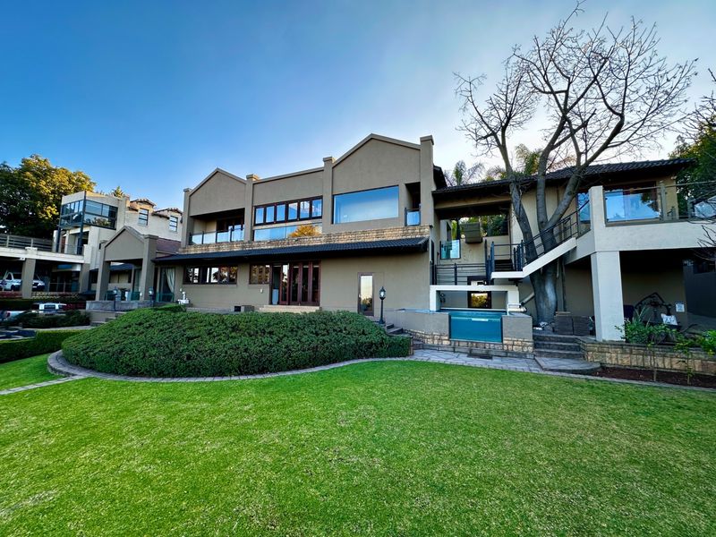 Rear view of a multi-level residence featuring a landscaped garden, swimming pool, stone-clad accents, and elevated balconies with large windows.