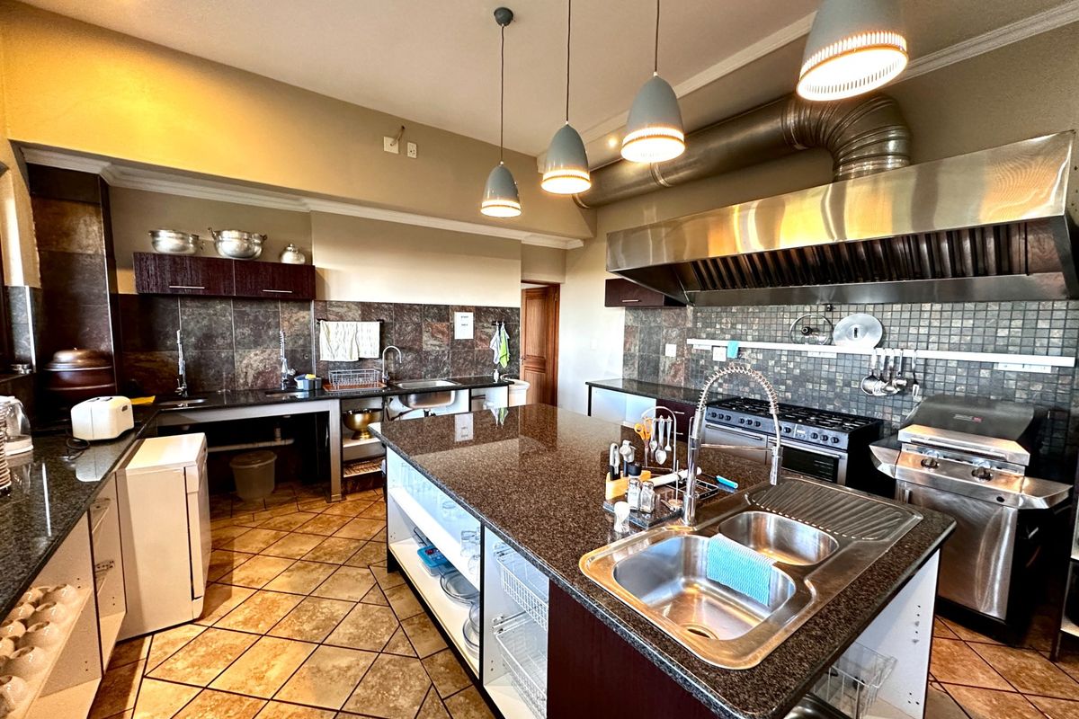 Spacious kitchen featuring granite countertops, a large central island with a double sink, industrial-style extractor hood, and ample built-in cabinetry.