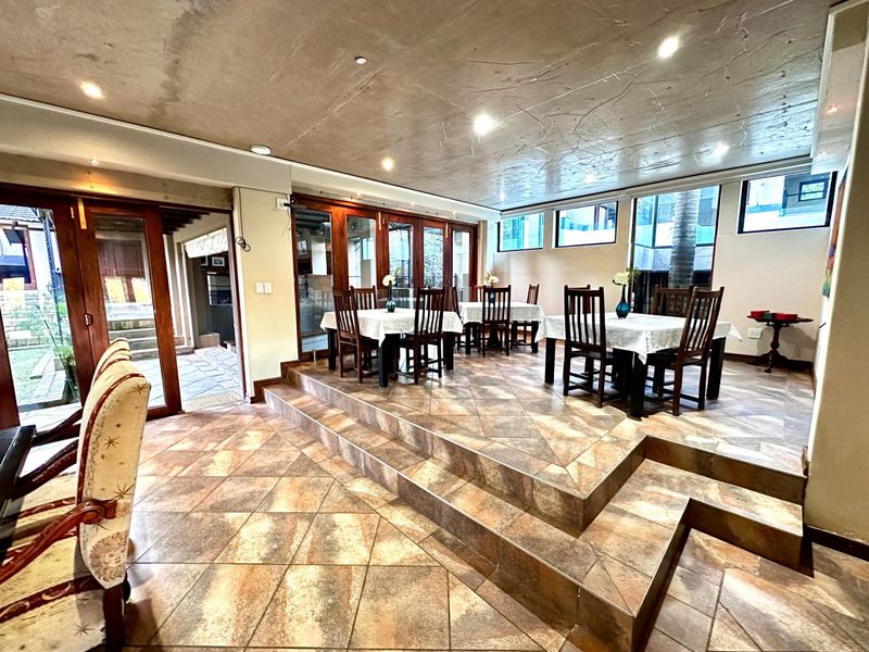 Spacious dining area featuring a raised tiled platform, recessed lighting, and large timber-framed glass doors providing access to the outdoor patio.
