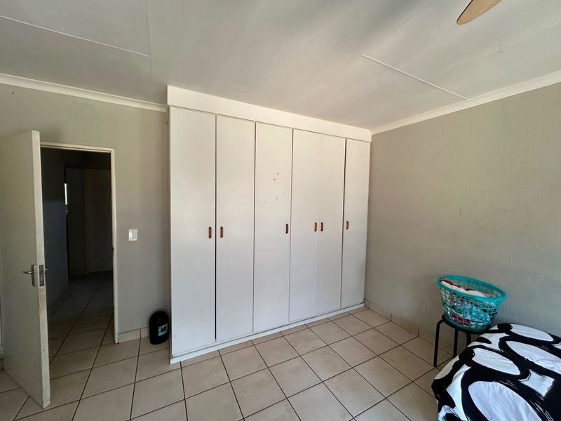 A bedroom featuring neutral tiled flooring and a large wall-to-wall built-in cupboard unit providing ample storage space.